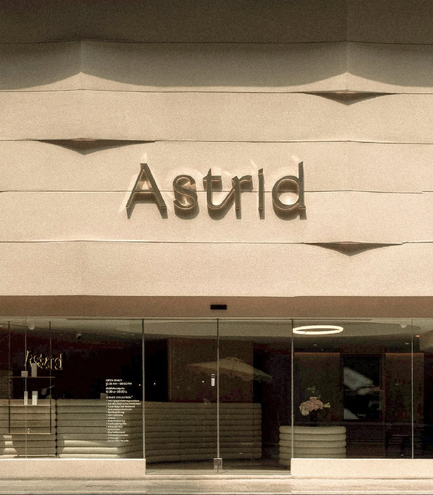 The front of the Astrid clinic, a curved cream facade with the Astrid name in raised letters above a glass shopfront and a reception desk inside