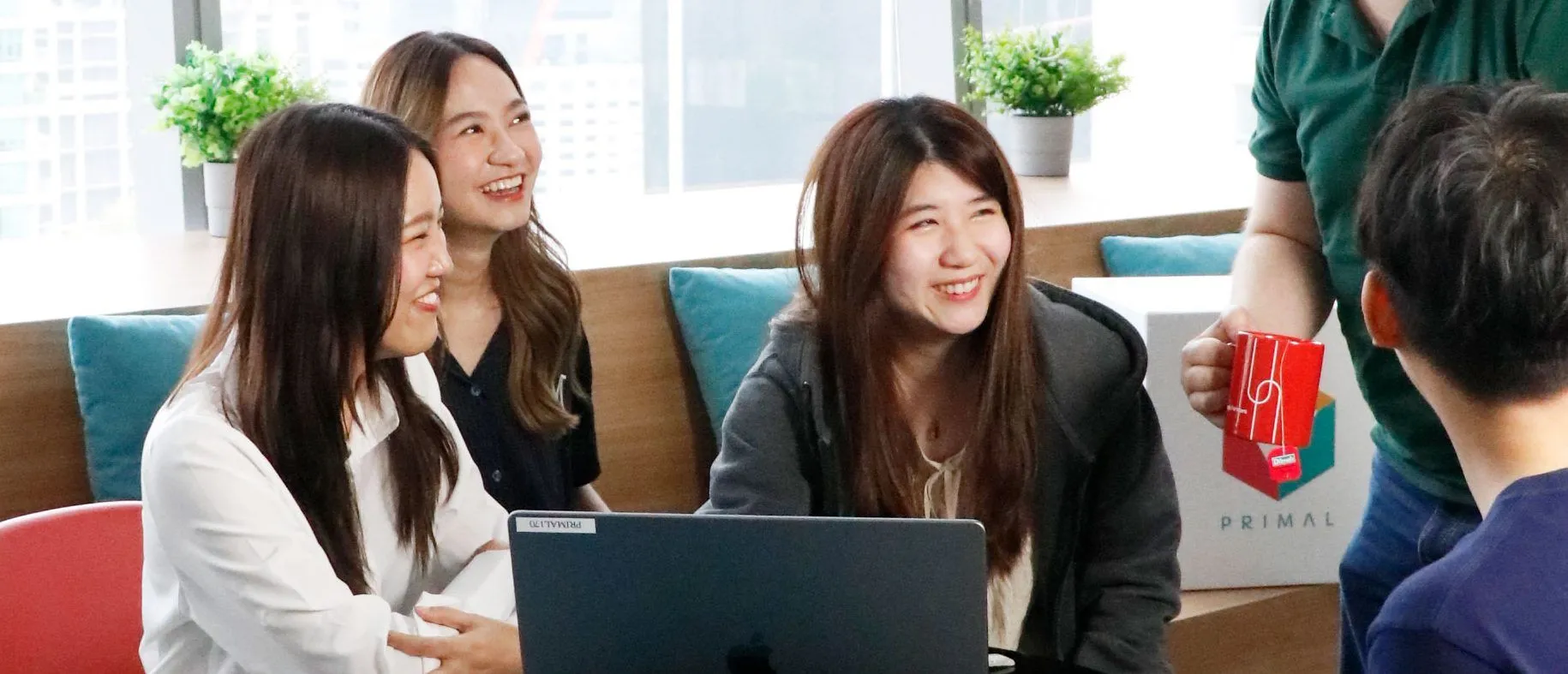 Primal colleagues smiling around a table with a laptop