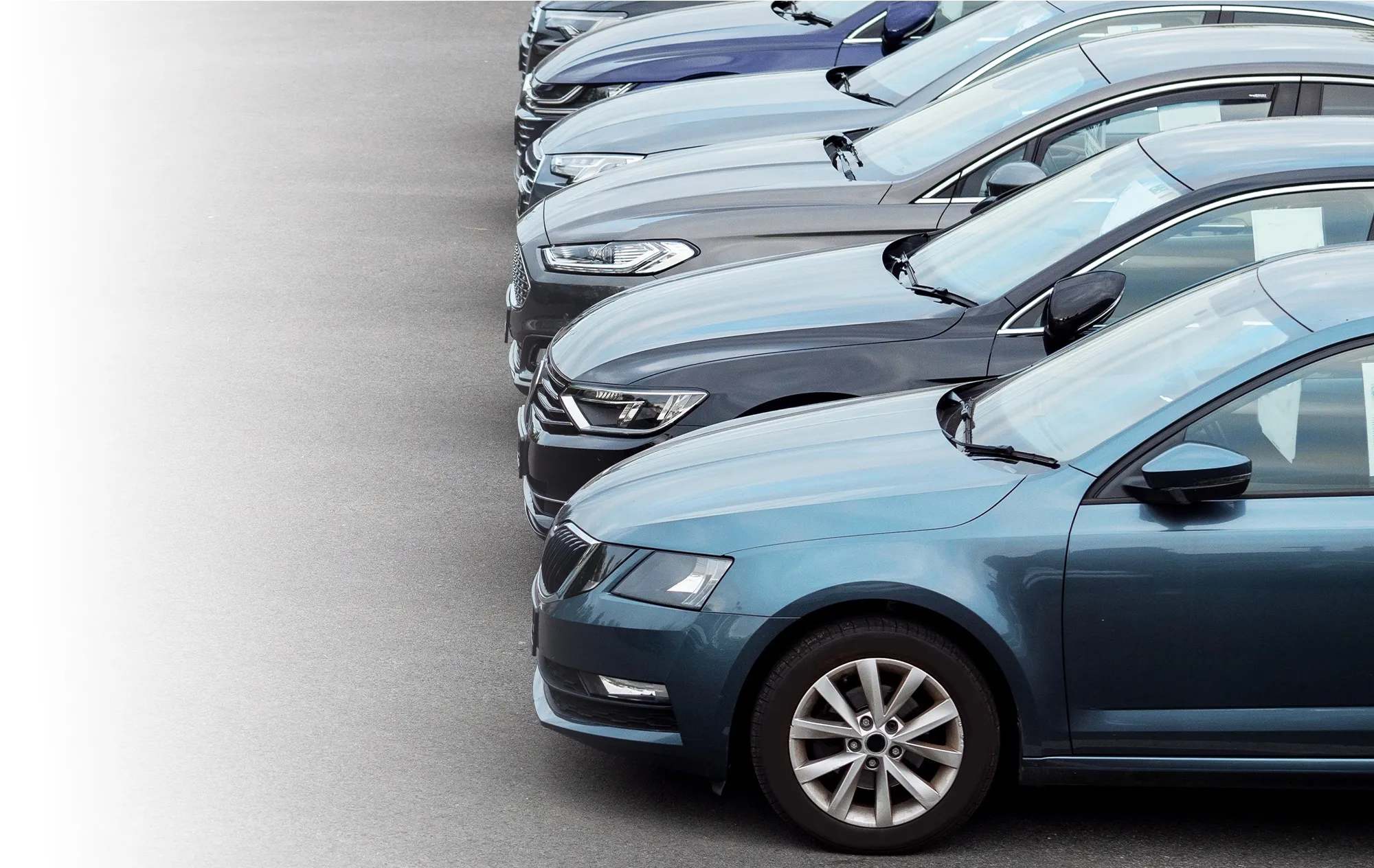 A row of parked saloon cars seen from the front corner, a blue-grey car closest
