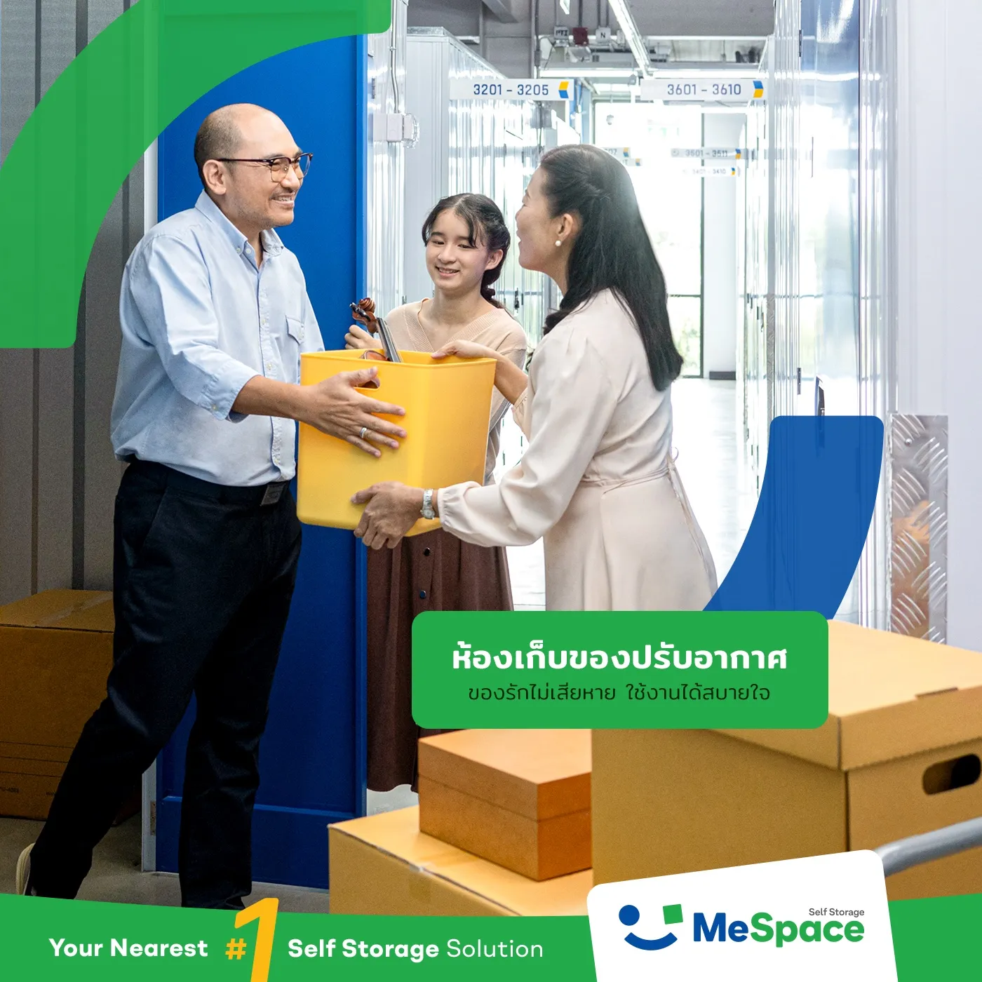 A smiling man in glasses passing a yellow box to a woman and a girl in a corridor of MeSpace storage units