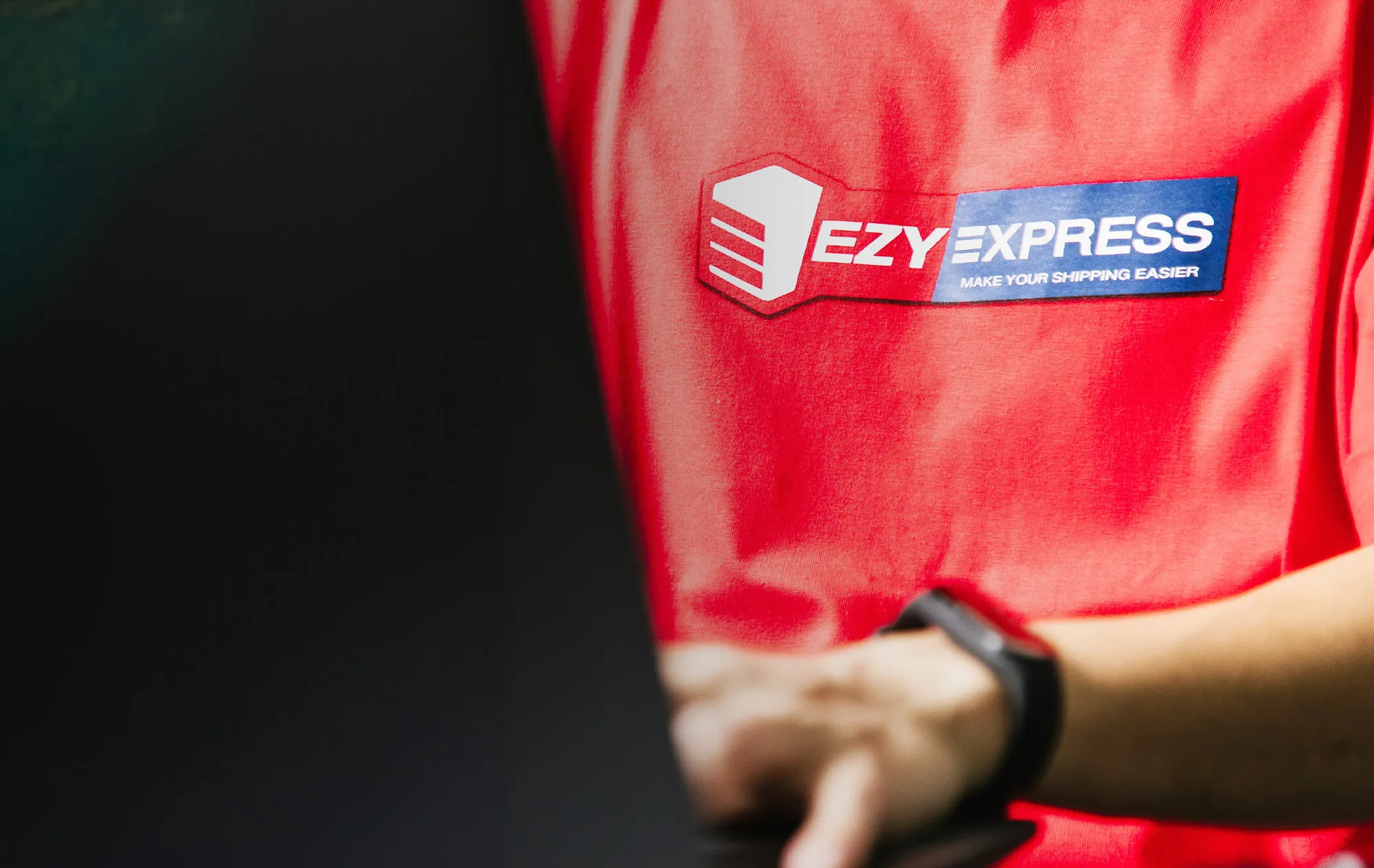 The Ezy Express logo on a red T-shirt, with a blurred hand and black watch strap in front