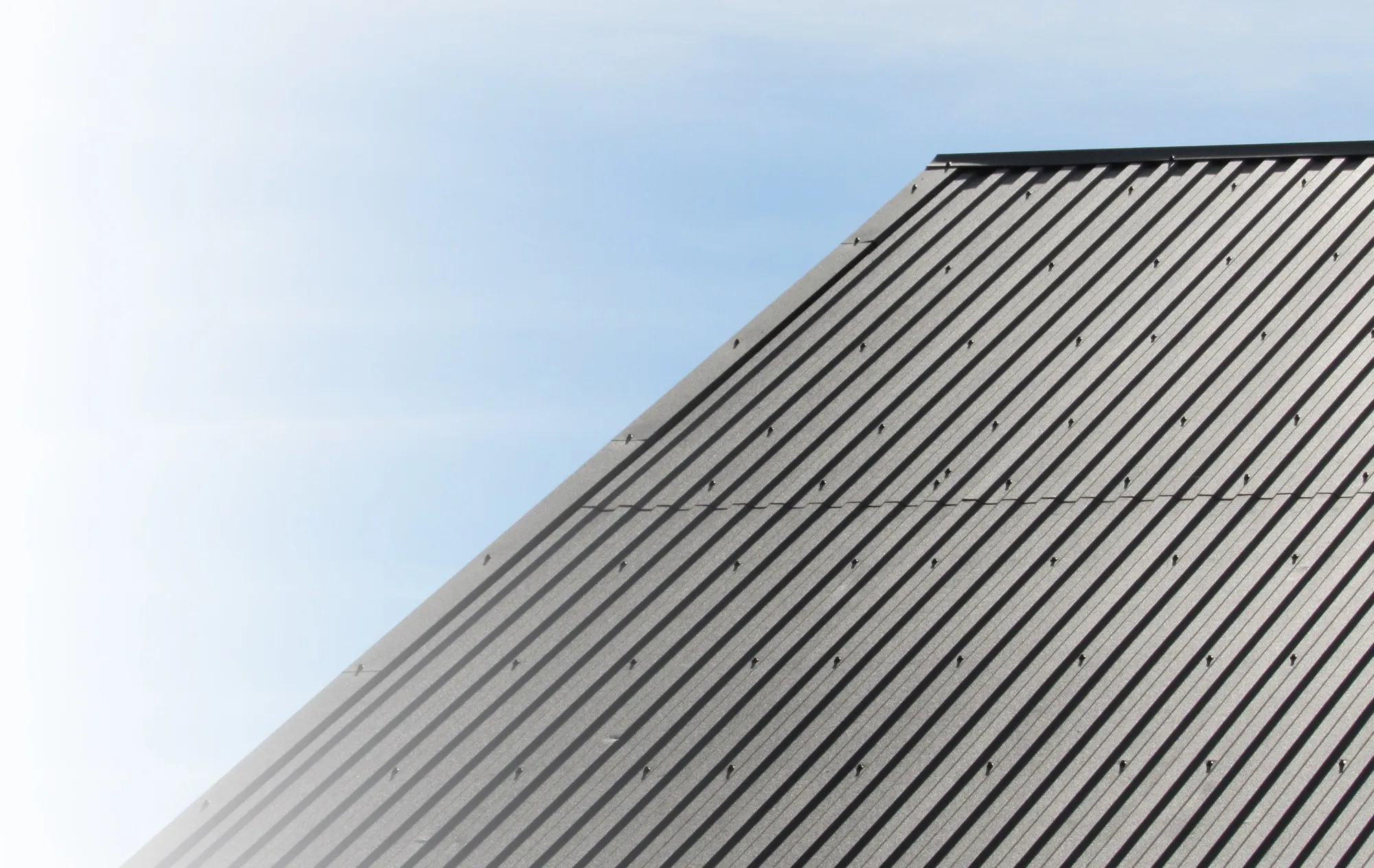 A dark grey ribbed metal roof rising at an angle against a pale blue sky