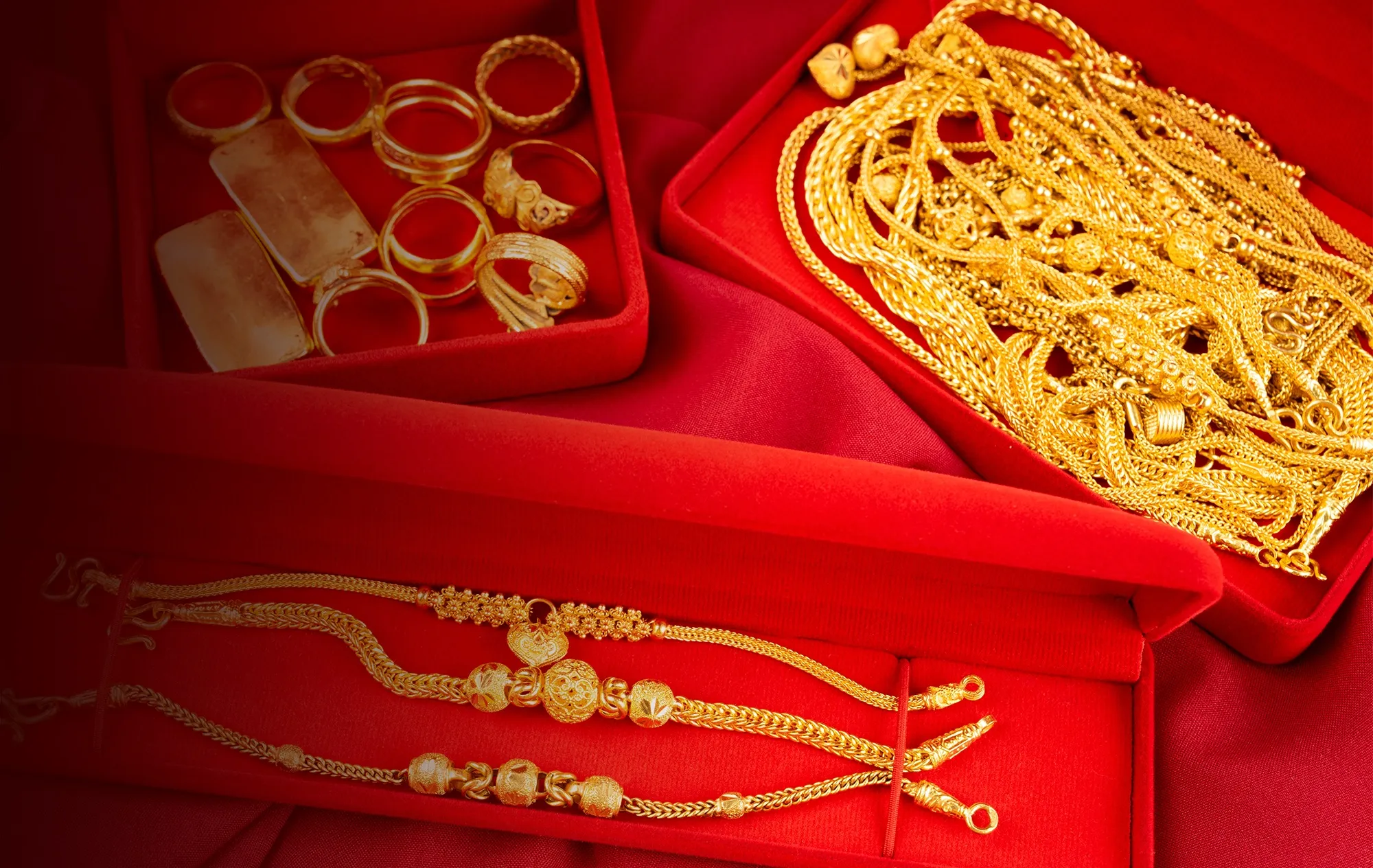 Gold rings, 2 flat gold bars, a heap of gold chain necklaces and 3 gold bracelets laid in open red velvet jewellery boxes