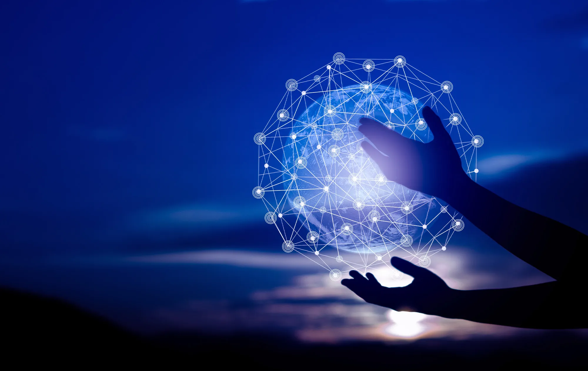 Two hands in silhouette around a glowing globe wrapped in a network of white lines and dots, against a dark blue evening sky