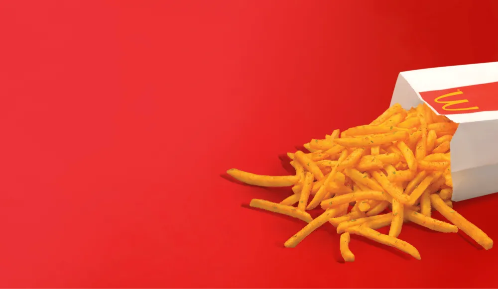 เฟรนช์ฟรายส์คลุกผงปรุงรสไหลออกจากถุงเฟรนช์ฟรายส์ McDonald’s บนพื้นหลังสีแดง