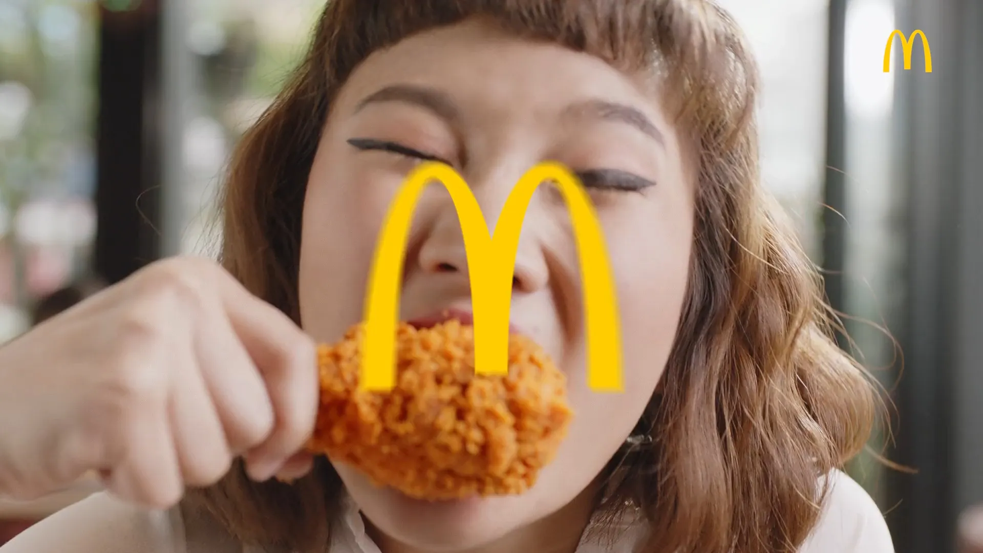 A woman eats a piece of McDonald’s fried chicken, with the golden arches over the picture