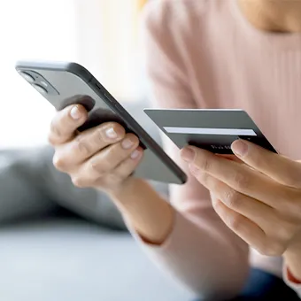 A woman holding a phone in one hand and a credit card in the other