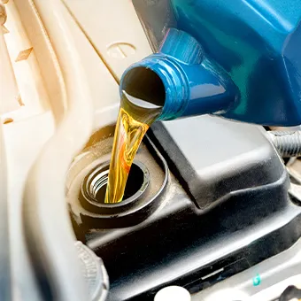 Golden engine oil pouring from a blue bottle into the filler opening of a car engine
