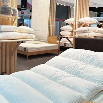 White pillows and quilted mattress toppers on wooden display stands