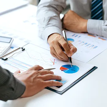 Two people at a desk pointing pens at pie charts and bar charts on printed reports