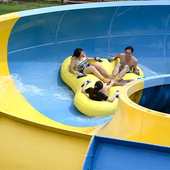 Two adults and a child on a yellow ring raft going round the curve of a blue and yellow water slide