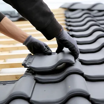 Hands in black gloves fitting dark grey roof tiles over wooden battens