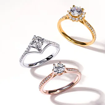 Three rings set with clear stones, one silver, one gold and one rose gold in colour, on a pale background