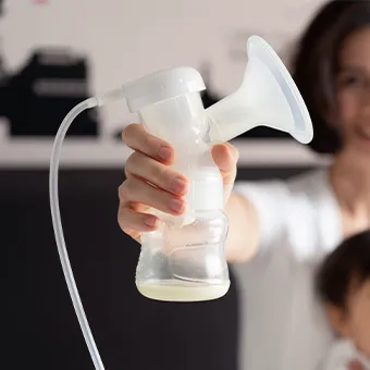 A smiling woman holding up a breast pump, a baby beside her