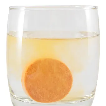 A round orange tablet dissolving at the bottom of a glass of water