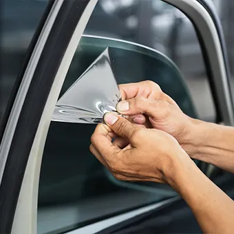 Two hands lifting the corner of a piece of window film on a car window