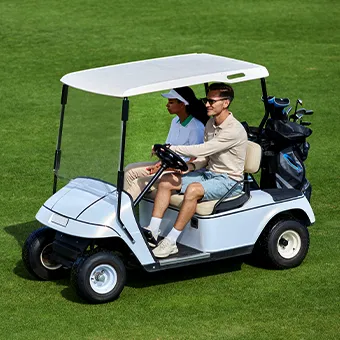 A man and a woman sitting in a white golf cart on a fairway, golf clubs in a bag behind them