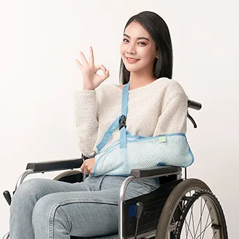 หญิงสาวยิ้มนั่งบนรถเข็น แขนข้างหนึ่งอยู่ในผ้าคล้องแขนสีฟ้า อีกมือทำสัญลักษณ์ OK
