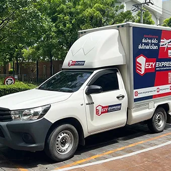 รถกระบะสีขาวของ Ezy Express ที่มีตู้บรรทุกสินค้า จอดอยู่บนถนนปูกระเบื้องข้างต้นไม้