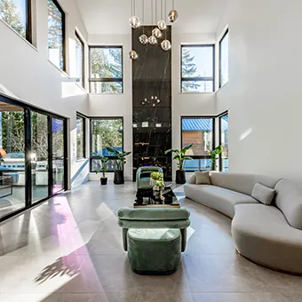 A double-height lounge with tall windows, a curved grey sofa and green velvet chairs
