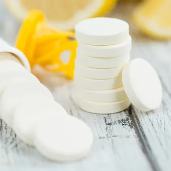 Round white tablets stacked and spilling from a white tube on a pale wooden table, lemon halves behind