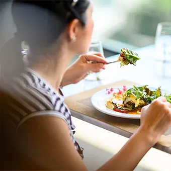 A woman in a striped top eating a salad with a fork at a table by a window