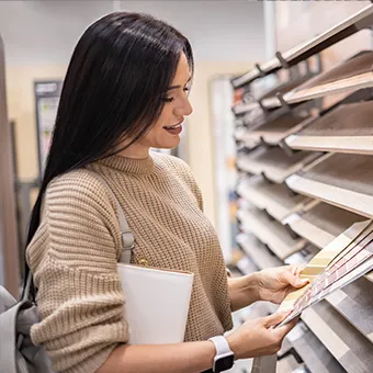 A smiling woman with a white bag looking at wood-effect samples on a showroom shelf