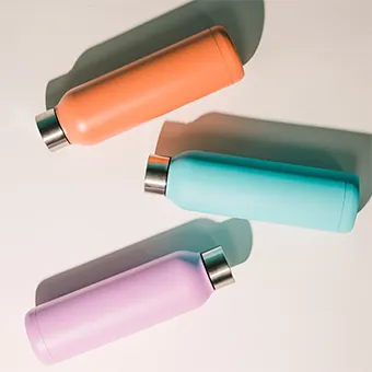 Three matte water bottles in orange, turquoise and lilac with steel caps, lying on a white background
