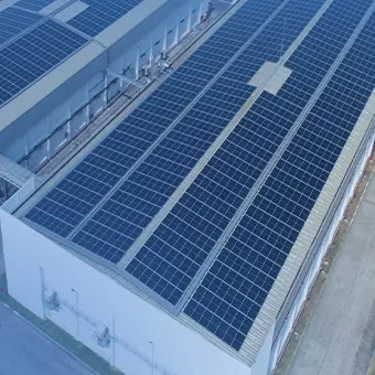 Rows of solar panels covering the roof of a large factory, seen from above