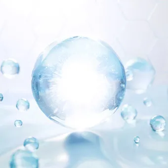 A clear glass sphere glowing with light among small water droplets on a pale blue background