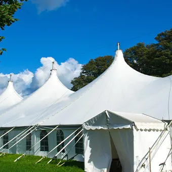 Large white peaked marquee tents on a green lawn under a blue sky, with trees behind