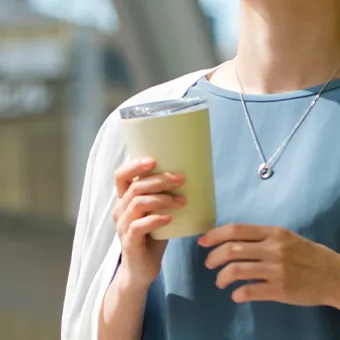 A woman in a blue top and a silver necklace holding a pale green cup with a clear lid