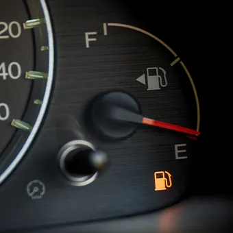 A car fuel gauge with the needle near E and the orange low fuel light on