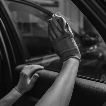A black and white photo of a gloved hand pressed flat against a car side window, another hand resting below the window
