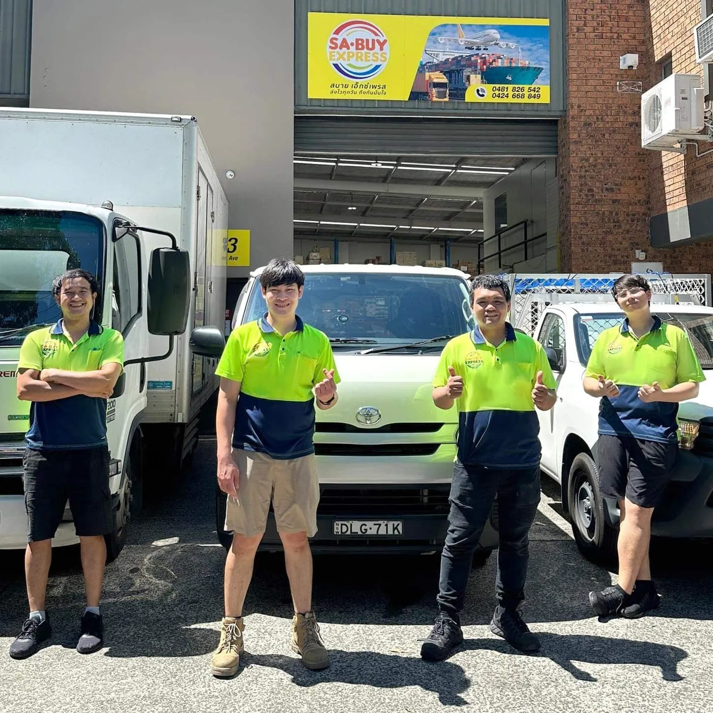 3 men in yellow-green and navy polo shirts make hand signs in front of a white van and a white pickup, under a yellow Sabuy Express sign above a warehouse entrance