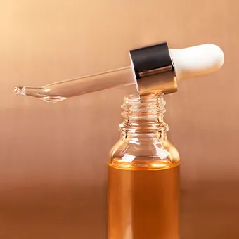 A glass dropper resting across the open neck of a small bottle of amber oil