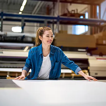 A smiling woman in a denim shirt smoothing a large white sheet on a table in a print workshop
