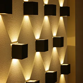 Square black wall lights casting beams of warm light up and down a textured wall