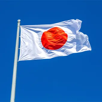 The Hinomaru, the red and white national banner of Japan, flying from a pole against a clear blue sky