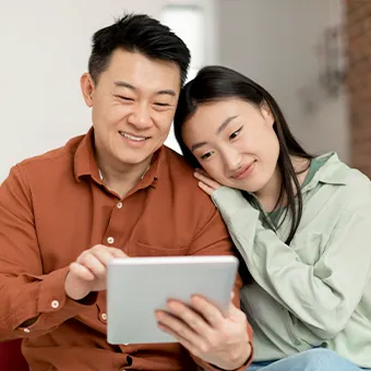 A man and a woman smiling at a tablet on a sofa