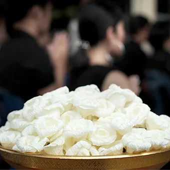 A gold bowl filled with white sandalwood flowers, people in black out of focus behind