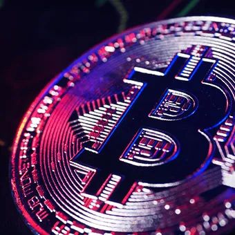 A close-up of a metal cryptocurrency coin lit in pink and purple