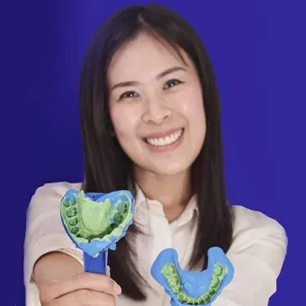 ผู้หญิงยิ้มยื่นถาดพิมพ์ฟันสีน้ำเงิน 2 ชิ้นที่มีวัสดุพิมพ์ฟันสีเขียว