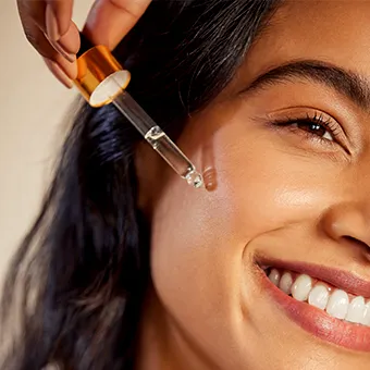 A smiling woman holding a glass dropper of serum against her cheek