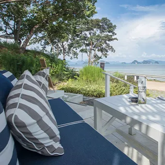 A navy sofa with grey and white striped cushions beside a white table on a terrace, looking over a garden to the sea and distant islands