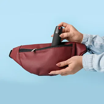 Hands putting a small black spray canister into a dark red waist bag