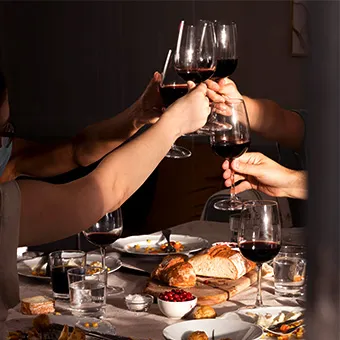 Friends raising glasses of red wine over a table with bread, small plates and a bowl of berries