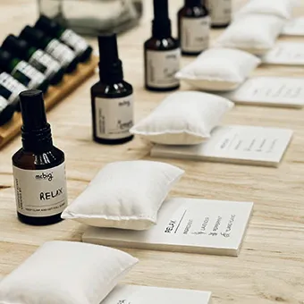 Dark glass bottles with mr.big RELAX labels beside small white pillows on cards, on a wooden table