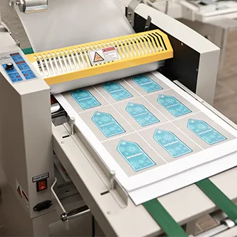 Sheets of printed blue tags passing through a finishing machine with a yellow guard