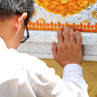 A man in a white shirt and glasses placing his hand on a gold and silver panel with Thai patterns